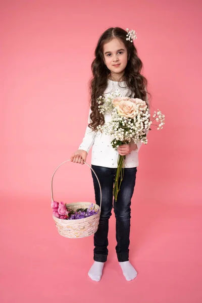 Glada brunett tonåring flicka i casual kläder håller bukett i höger hand och korg med våren blommor i höger hand, tittar på kameran — Stockfoto