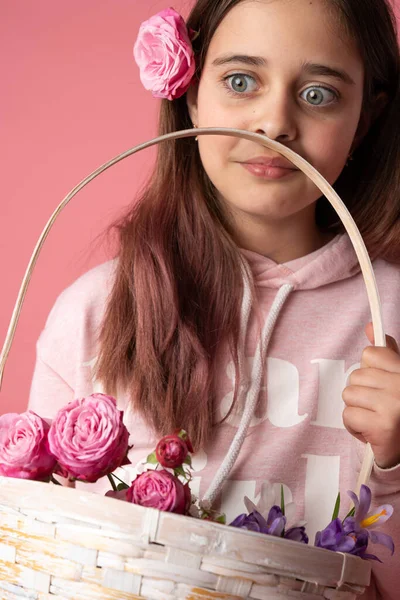 Överraskad brunett flicka i rosa hoodie innehav korg med vårblommor, hona med blomma i håret — Stockfoto