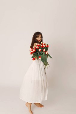 Beyaz elbiseli mutlu esmer kadın ellerinde lalelerle kameraya bakıyor, 8 Mart