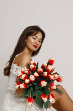 Beyaz elbiseli bir kızın portresi beyaz arka planda izole edilmiş büyük bir lale buketi tutuyor.