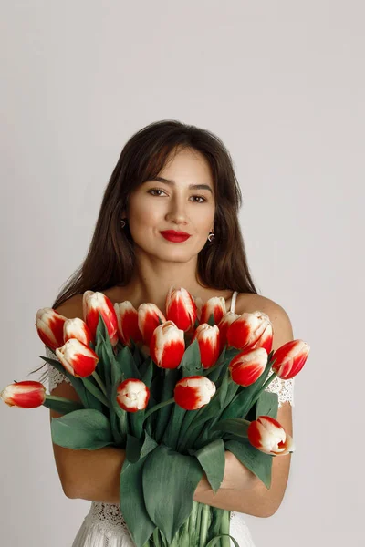 Gros plan femme brune heureuse avec des lèvres rouges tenant bouquet de tulipes rouges et regardant la caméra — Photo