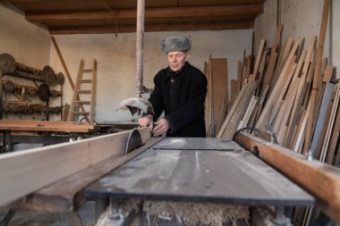 Çok yaşlı marangoz atölyesinde tahta kesiyor.