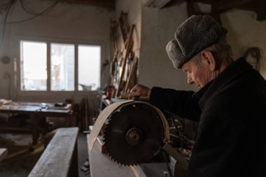 Kıdemli marangoz günlük giysiler içinde elektrikli testere kullanıyor. Atölyesinde çalışıyor.