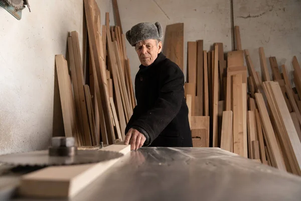 Carpintero viejo europeo que trabaja en la mesa de trabajo de madera en la carpintería casera. Viejo hombre europeo trabaja en carpintería . — Foto de Stock
