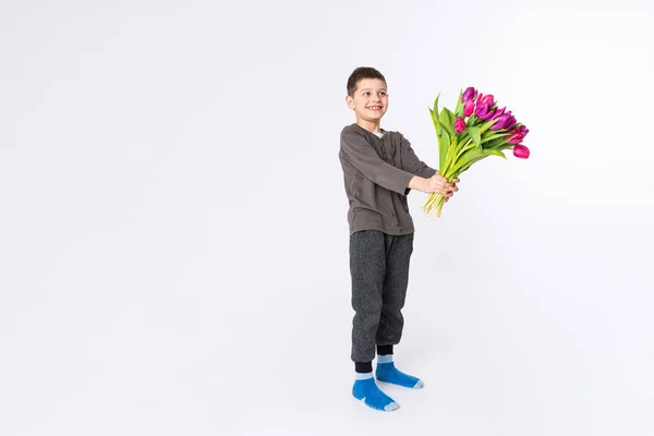Glada lilla brunett pojke ger bukett av röda tulpan blommor på vit studio bakgrund. Gåvor blomma leverans, vår kvinna dag. — Stockfoto