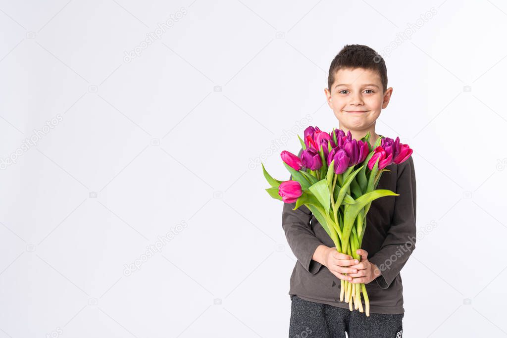 Happy little boy in casual clothes with a bouquet of tulips isolated on white background, looks at camera
