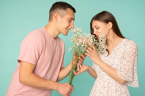 Attractive young couple in casual clothes holding together bouquet and smelling flowers with closed eyes — Stock Photo, Image
