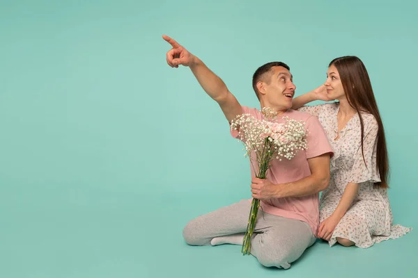 Hermosa joven feliz pareja emocionada en el amor sonriente abrazar dedo de punta para vaciar el espacio de copia, hombre y mujer mirándose, chico sostiene flores — Foto de Stock