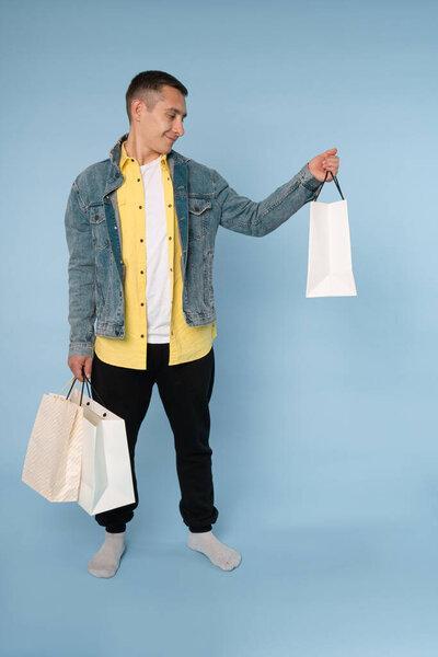 Stylish young man in blue jeans jacket holding shopping bags in his hands and looking at it