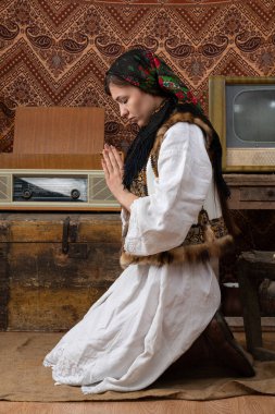 Ulusal giysili genç Ukraynalı kız eski moda retro odasında diz çöküp dua ediyor.