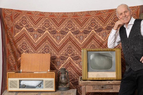 Удовлетворенный старик в элегантной одежде опирался на ретро-телевизор и смотрел в камеру — стоковое фото