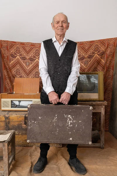 Stylish elder man in white shirt holds travel valise in his hands and looking at the camera