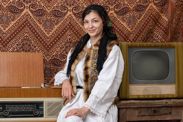 Art portrait of young woman in national clothes standing in room with vintage wallpaper and interior with tv and radio — Stock Photo, Image