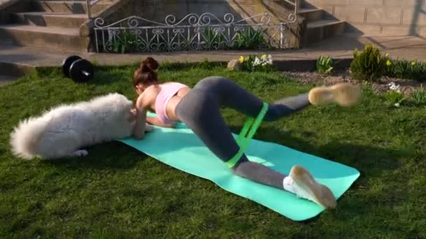 Junge Frau in Sportbekleidung macht draußen auf blauer Yogamatte Übungen mit Widerstandsband — Stockvideo