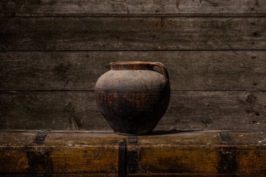 Antik kil vazo soğuk tonlu, ahşap masa üzerinde duruyor, yaşlanmış ahşap duvar.