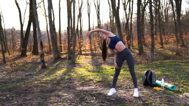 Donna che fa esercizi di fitness all'aperto. Corridore donna che si allunga prima di correre maratona nella foresta verde. Slim ragazza in abiti sportivi facendo esercizi di stretching nel parco . — Video Stock