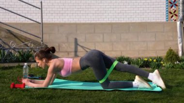 Gri taytlı ve pembe ayaklı bir kız. Evdeki yoga minderinin üzerinde yeşil bir direnç bandı var.