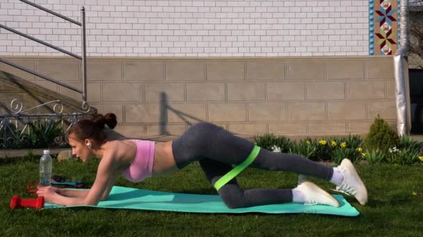 Vrouw die traint voor benen met een elastische band op de vloer op de yogamat — Stockvideo