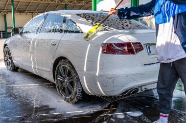 Günlük giysiler içinde lüks arabaları yıkayan bir erkek işçi..