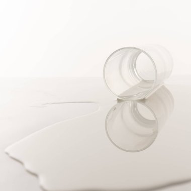 Sütlü eğimli bir bardak beyaz bir masanın üzerinde yatıyor.