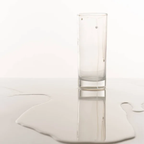 Boş bardak masanın üzerine dökülen sütün arasında duruyor. — Stok fotoğraf