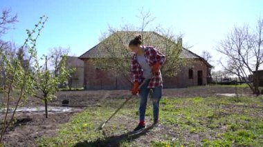 Çekici, neşeli esmer kız günlük giysiler içinde bahçede yaprakları tırmıklıyor.