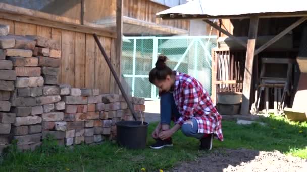 Aantrekkelijk brunette meisje in de achtertuin strikken schoenveters en het nemen van werkhandschoenen uit de emmer — Stockvideo