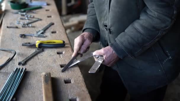 Старий чоловік відполірує металеву пластину на робочому столі вдома — стокове відео