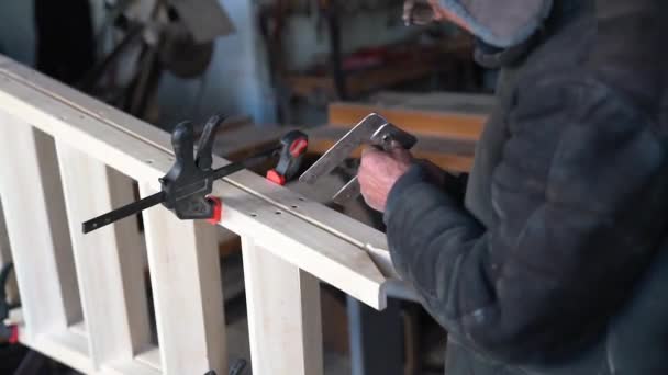 Stolarz Pencioner w okularach przymierza metalową płytę do drewnianej drabiny — Wideo stockowe