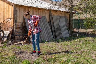 Yan görünüşte, esmer saçlı, ekose gömlekli güzel bir kız. Arka bahçede tırmıklarla çalışıyor.