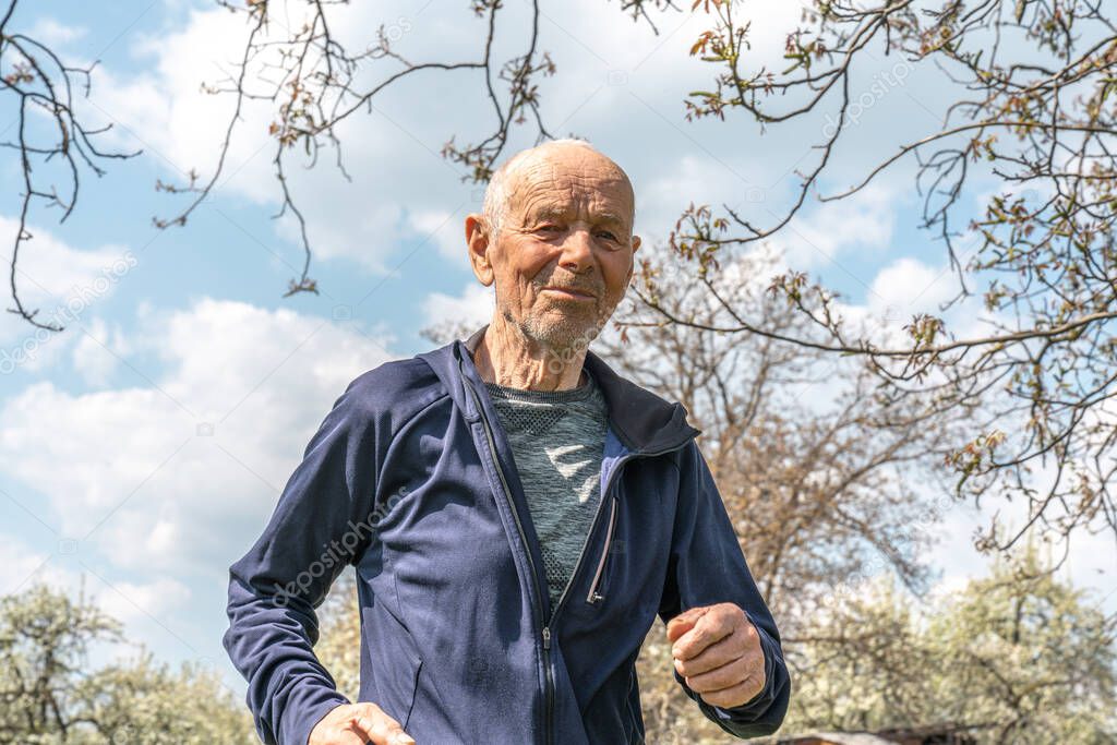 90 years old man in sportswear running among blooming garden during spring sunny day