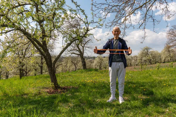 Старый европейский человек растягивает мышцы в концепции тренировки дома с бандой сопротивления . — стоковое фото
