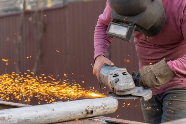 Zanaatkar arka bahçede disk öğütücüyle metal kesiyor.