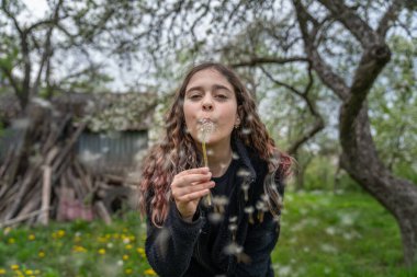 Çekici esmer kız kameraya karahindiba üflüyor.