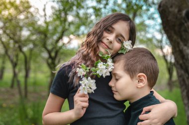Çekici esmer kız çiçek açan bir dal tutuyor ve küçük kardeşine sarılıyor.