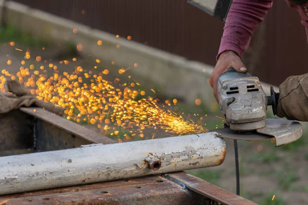 Un soldador joven procesa un producto metálico con una amoladora angular en el garaje —  Fotos de Stock