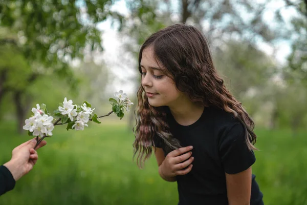 Tender brunett flicka i svart t-shirt lutade mot blommande gren i pojkar hand — Stockfoto