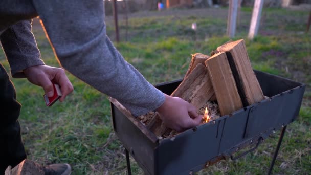 Un homme allume un feu dans un brasero avec des allumettes . — Video