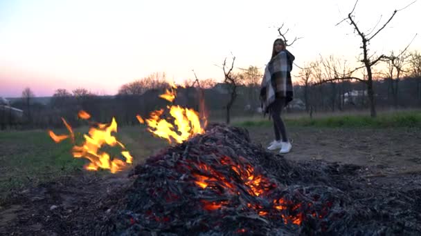 Attraktives junges Mädchen in ein Plaid gehüllt, das hinter einem Lagerfeuer im Hinterhof steht — Stockvideo
