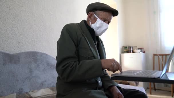 Senior man zit aan het bureau en draagt een chirurgisch masker, hij verbindt zich met zijn laptop en streamt een video online op zijn kanaal — Stockvideo