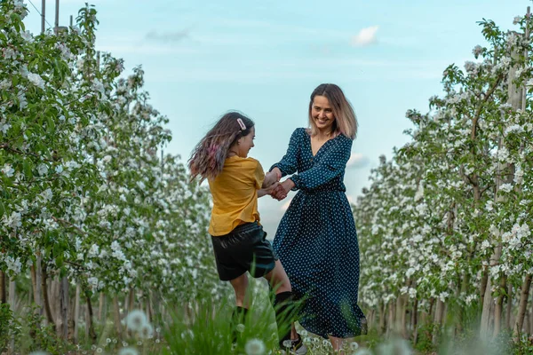 Szczęśliwy piękny mama i córka w eleganckie ubrania taniec wśród kwitnącego ogrodu — Zdjęcie stockowe