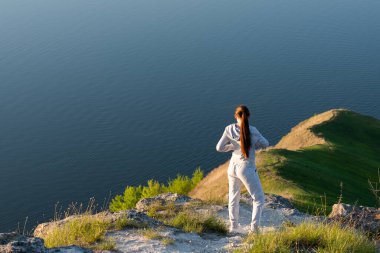 # Kız, yeşil ağaçlarla çevrili # # altında mavi bir nehir olan # # kanyona bakan bir kayanın üzerinde duruyor #