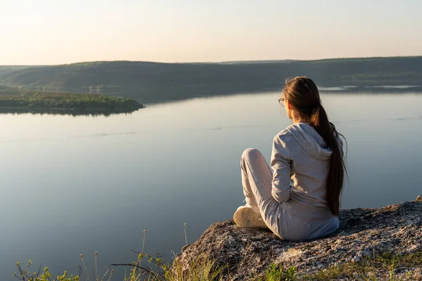 바위 위에 앉아 강이 흐르는 골짜기 밑을 바라보고 있는 소녀 — 스톡 사진