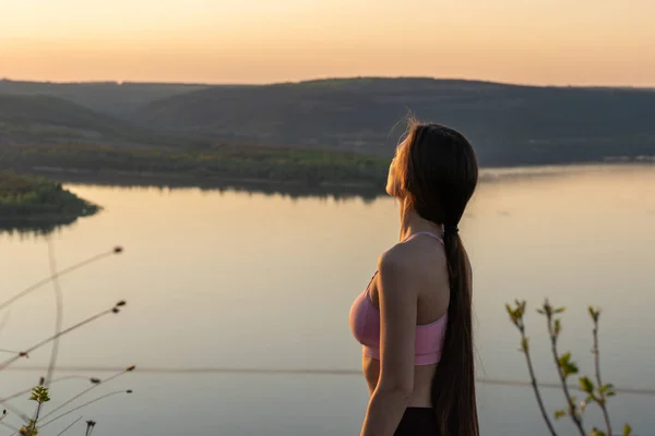 갈색긴 머리를 한 젊은 여자가 분홍색 브라를 입고 멀리 서 산 과 강을 바라보고 있습니다. — 스톡 사진