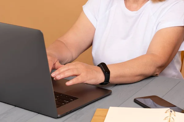 Close up de uma mulher sentada na frente de seu computador portátil, telefone à mesa e mãos no teclado na sala — Fotografia de Stock