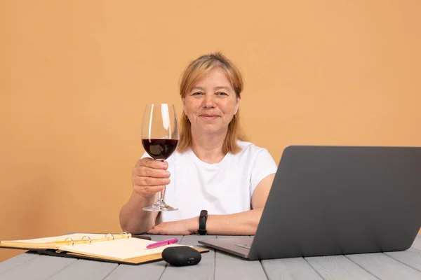 Technology, old age and people concept - happy senior woman in white t-shirt with laptop computer and glass of wine at home