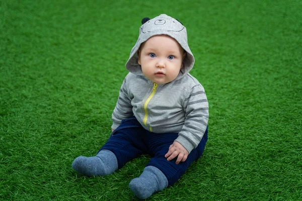 Little beautiful child sits on a green lawn and looks in surpris — ストック写真