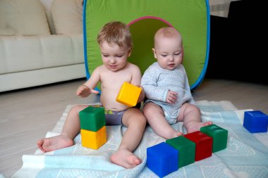 Küçük çocuklar yerde oturup küp oynayarak eğleniyorlar. Chi