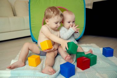 Küçük çocuklar yerde oturup küp oynayarak eğleniyorlar. Chi