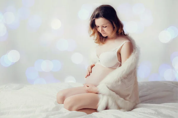 Uma bela mulher grávida está sentada em sua cama e olhando para — Fotografia de Stock